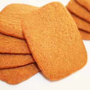 Une pile de biscuits Spéculoos rectangulaires de couleur gingembre, disposés sur un fond blanc.