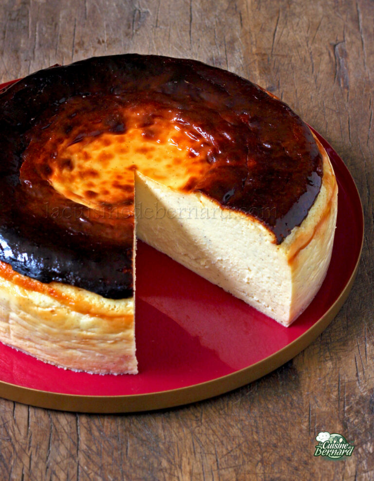 A Basque burnt cheesecake with a slice cut out, showing the creamy interior. The top of the cheesecake is caramelized, and it is placed on a red plate against a wooden background.