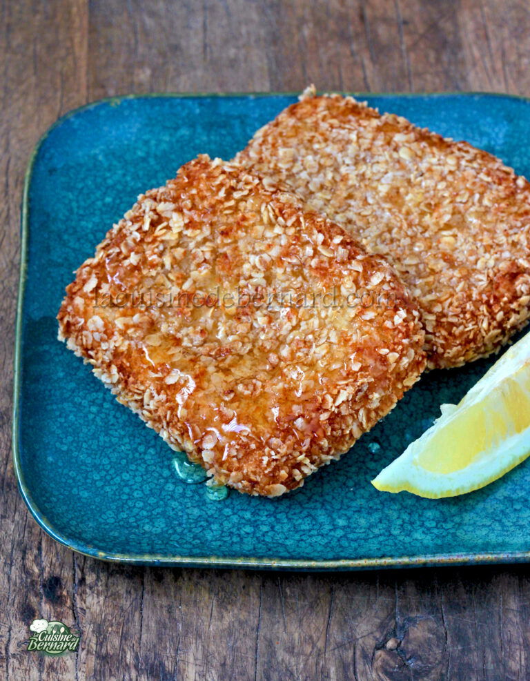 Two breaded fish fillets on a green ceramic plate with a lemon wedge, presented on a wooden surface.