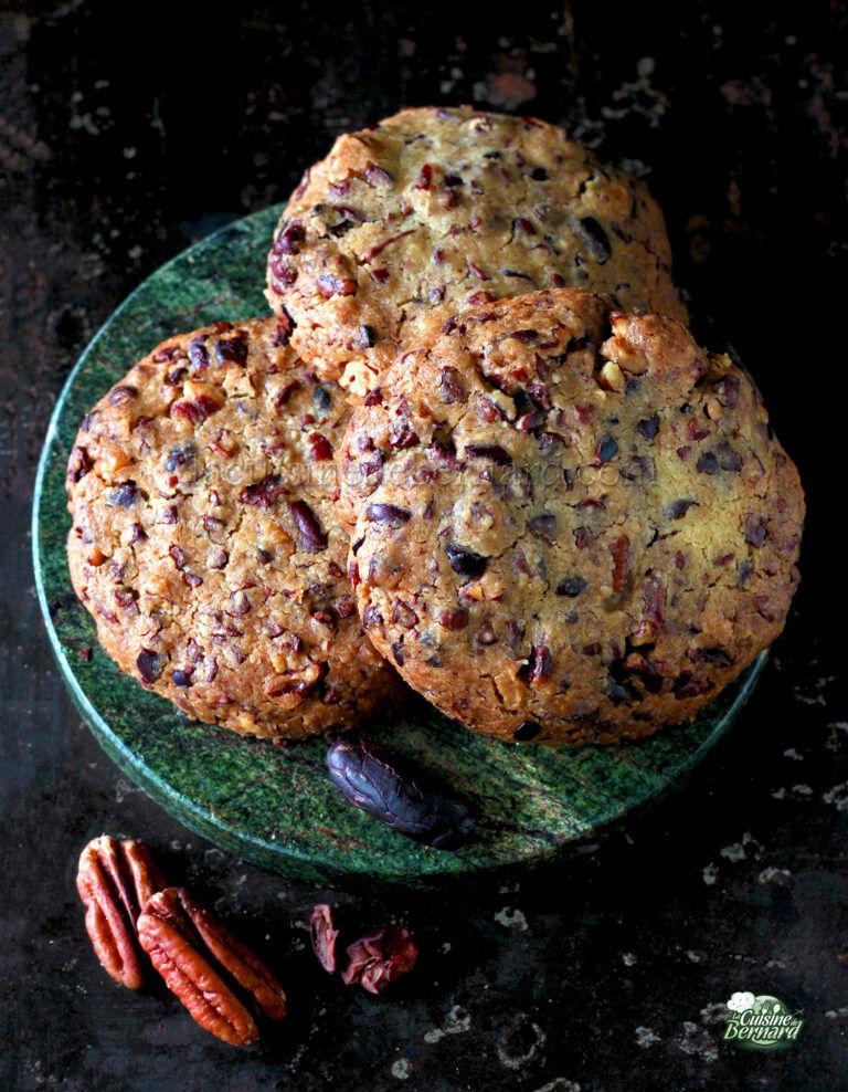Three large oatmeal cookies with pecans and cranberries on a green plate, set against a dark background.