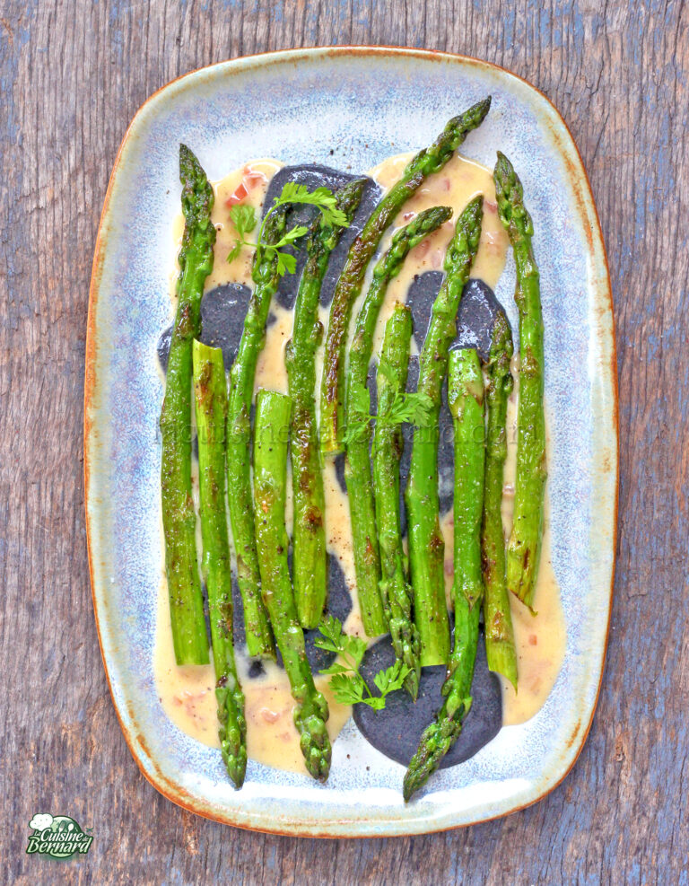 Asperges grillées à la perfection, servies sur une assiette bleue et arrosées d'une riche sauce au beurre blanc, garnie d'herbes fraîches.
