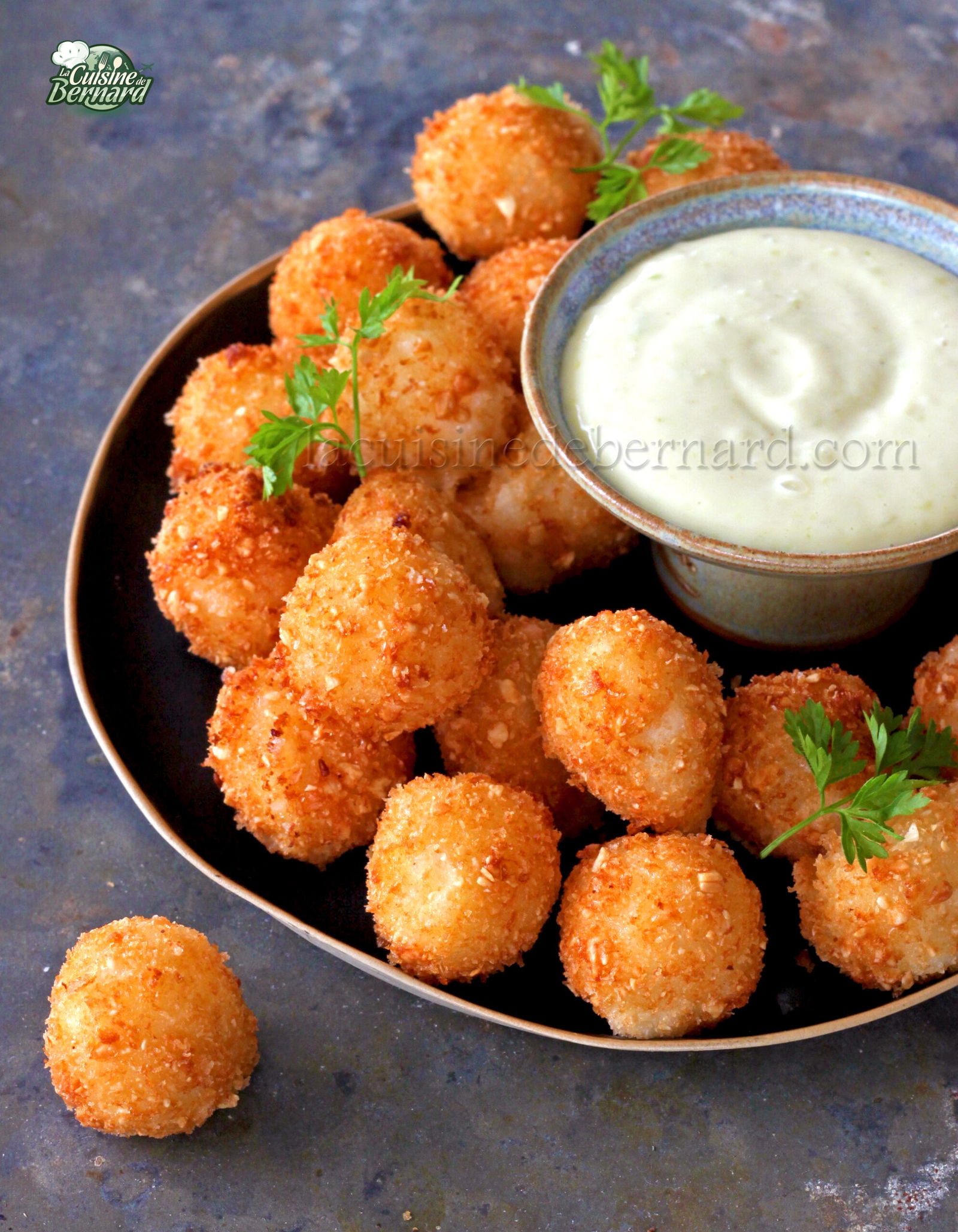 Um prato de bolinhas douradas de Mozza decoradas com salsa, servidas com uma tigela pequena de molho cremoso de maionese de wasabi.