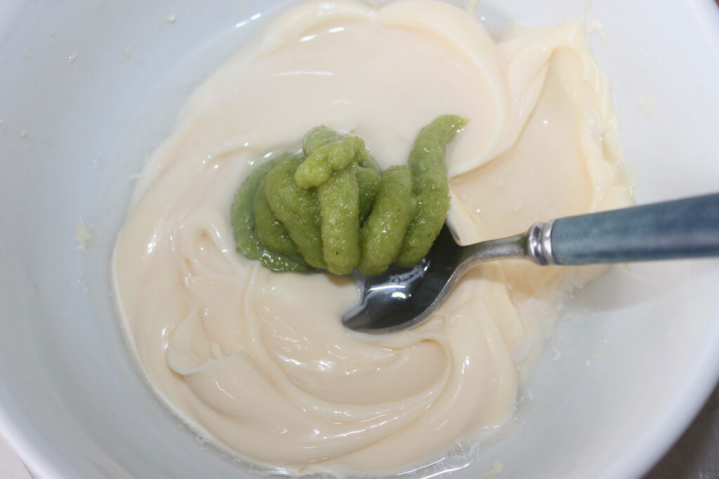 Uma tigela contendo uma mistura de maionese branca e wasabi verde, com uma colher dentro.