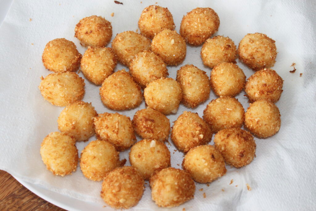 Um prato coberto com um guardanapo de papel branco contendo várias bolas Mozza marrom-douradas, espaçadas uniformemente, sugerindo um tipo de alimento empanado e frito.