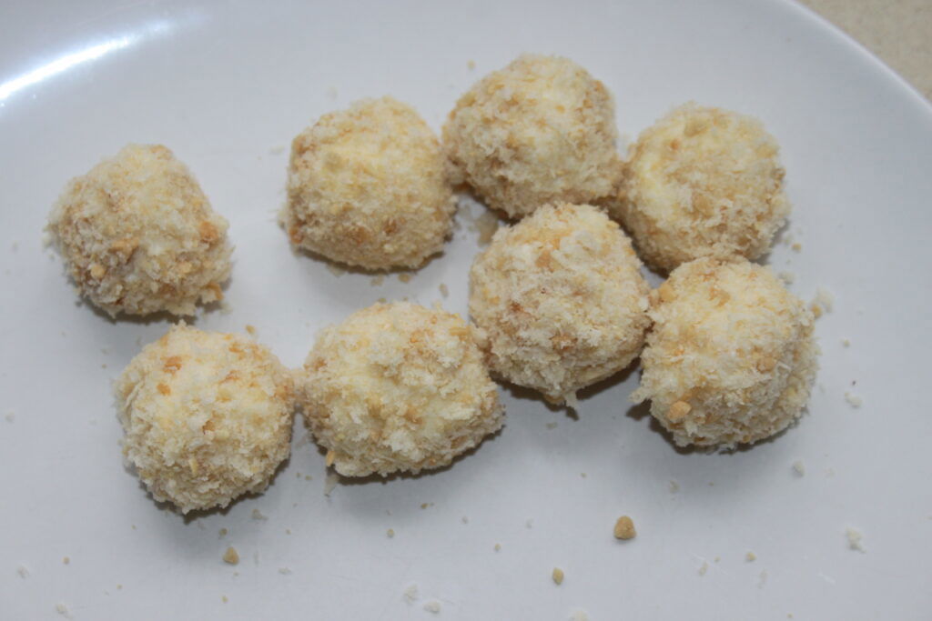 Oito bolas de Mozza empanadas e fritas dispostas em um prato branco, perfeitamente complementadas por um acompanhamento de maionese de wasabi.