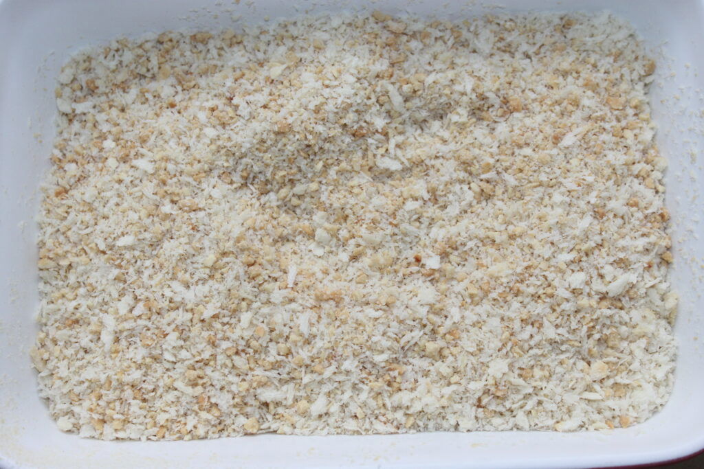 Close-up de um recipiente retangular branco cheio de farinha de rosca finamente moída, perfeito para cobrir as deliciosas bolas de Mozza.