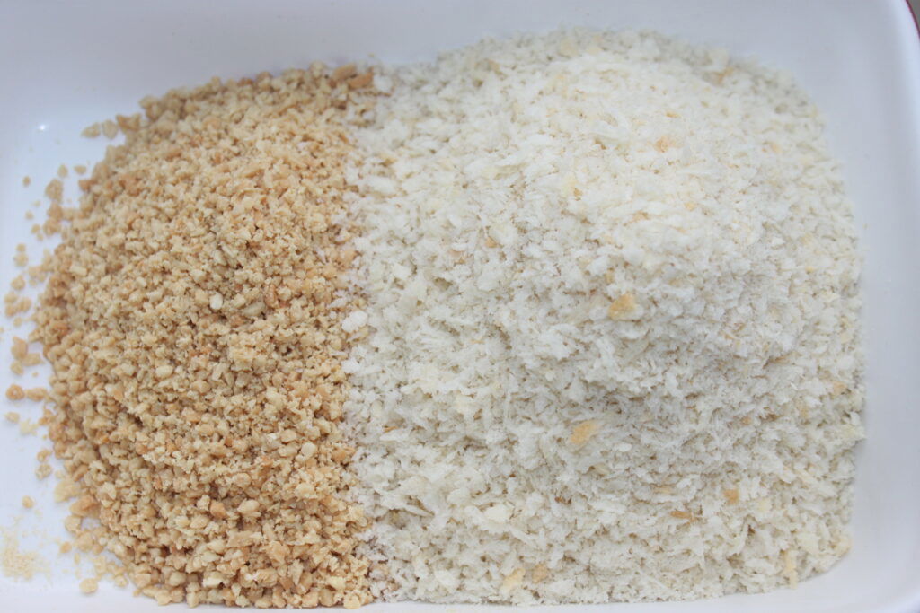 Um close-up de duas pilhas distintas de migalhas de pão em uma superfície branca; a pilha da esquerda é dourada e a pilha da direita é leve e fofa, lembrando as texturas encontradas nas bolas Mozza ou na preparação de mordidas crocantes com um toque de maionese de wasabi.