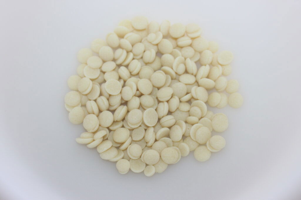 Un tas de petites tablettes ou pastilles rondes, blanc cassé, sur une surface blanche unie, rappelant les ingrédients raffinés que l'on trouve dans le chocolat de luxe tel que le Chocolat de Dubaï.