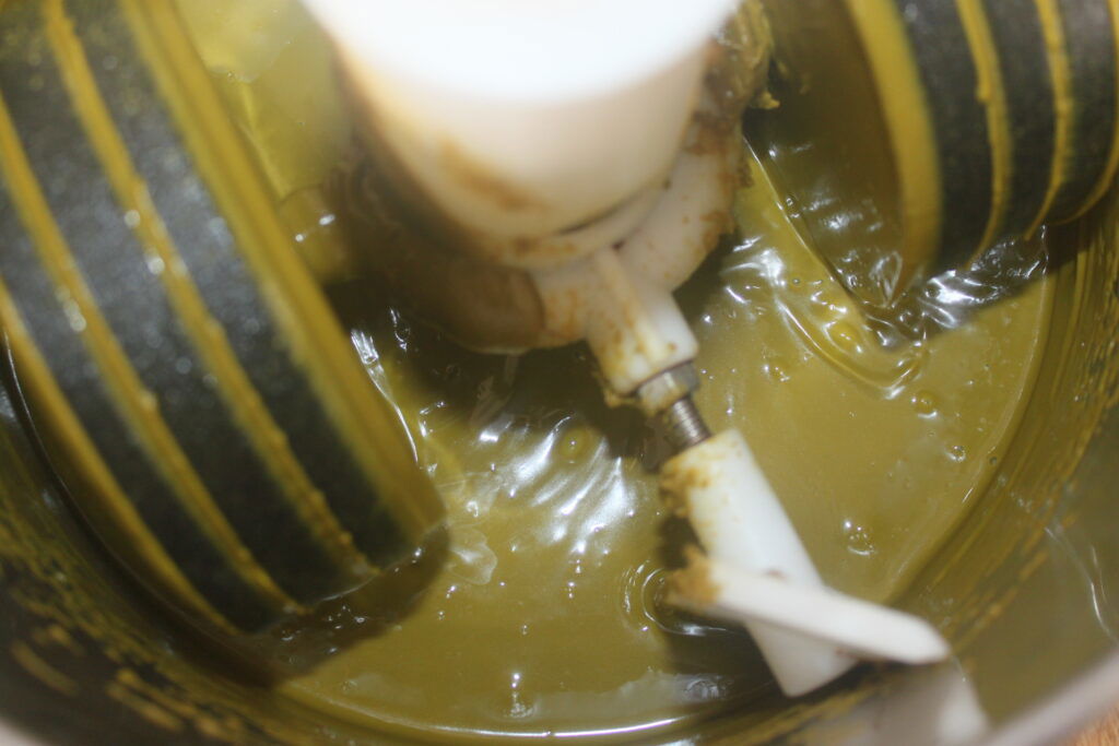 Gros plan d'un robot culinaire mélangeant une pâte verte épaisse, peut être une sauce ou une pâte à tartiner, avec des lames en plastique visibles parfait pour préparer des garnitures ou des pâtes à tartiner à associer aux délices du Chocolat de Dubaï.
