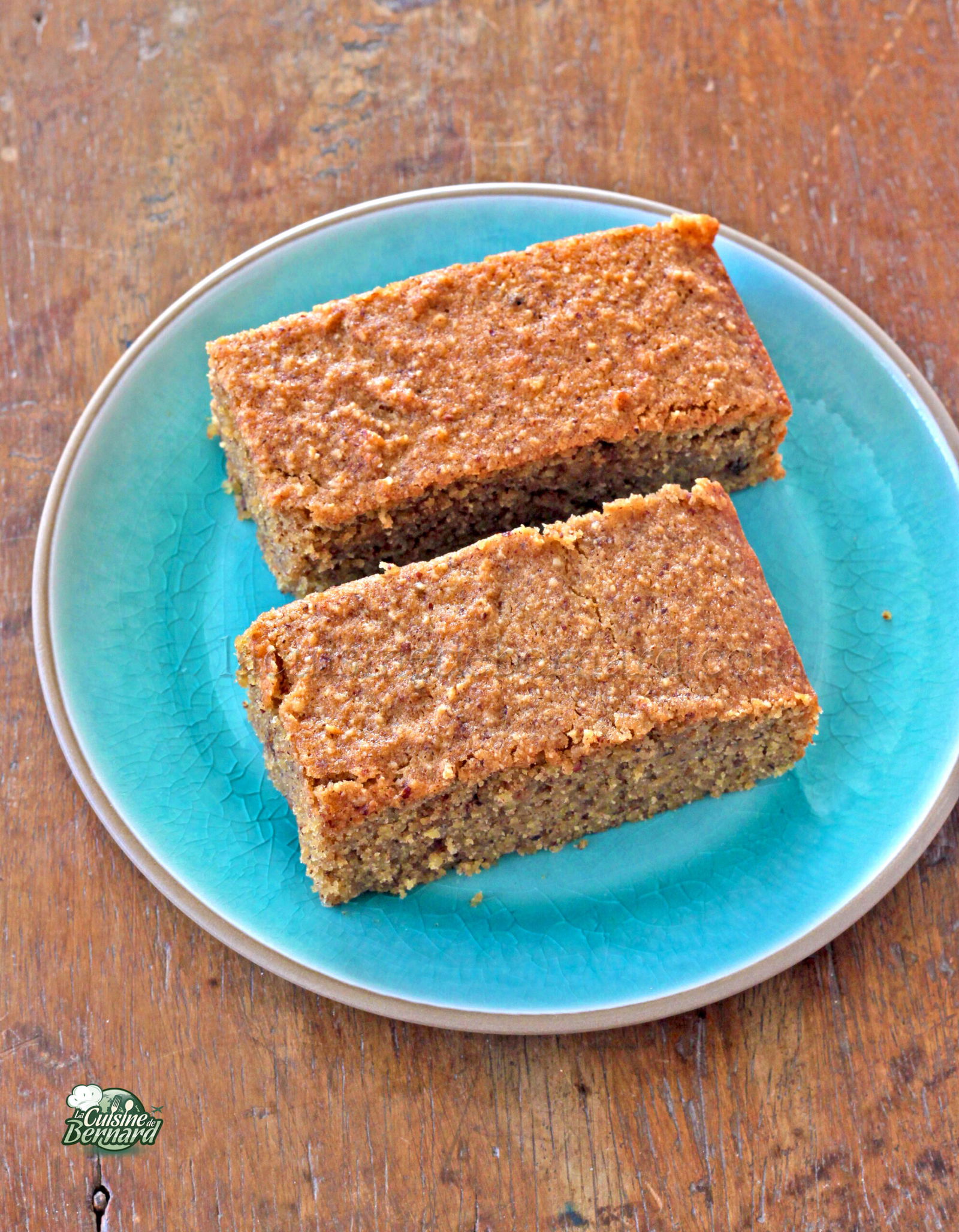 Deux tranches rectangulaires de gâteau financier sont posées élégamment sur une assiette bleue, posée sur une table en bois rustique.