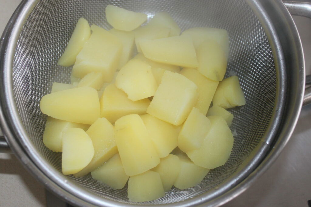 Morceaux de pommes de terre cuits à la vapeur dans une passoire en métal, rappelant le moelleux des petits pains moelleux parfaits.
