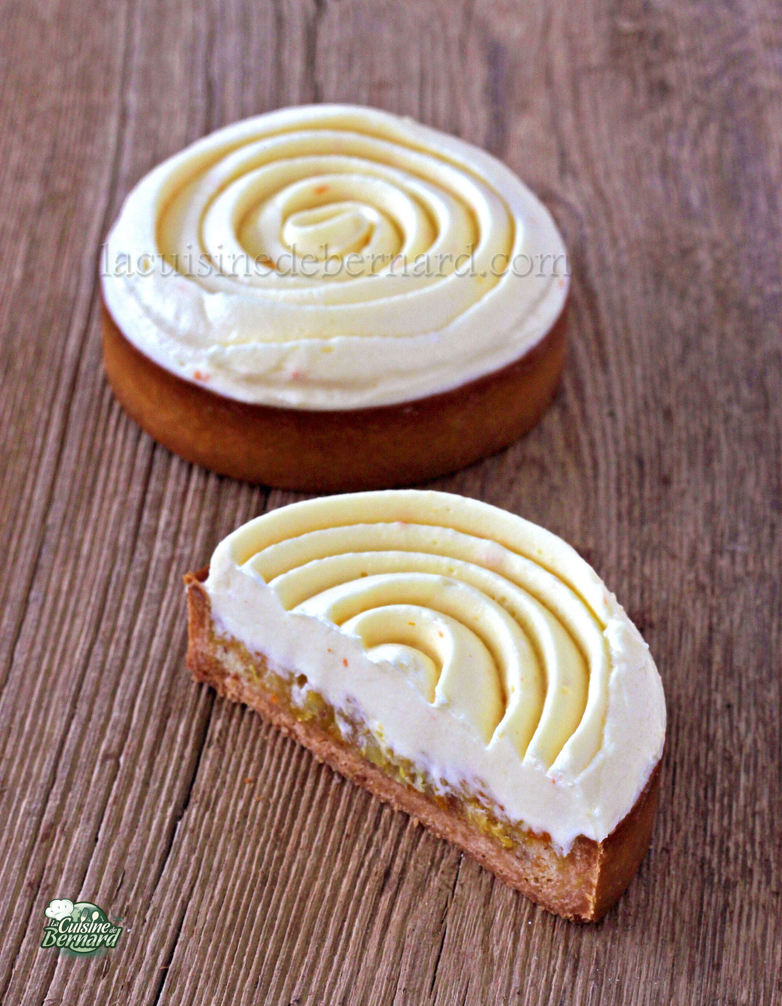 Une tarte et une pâtisserie sont posées sur une surface en bois, chacune ornée d'un glaçage blanc en spirale ; la tarte est coupée en deux pour révéler un intérieur crémeux et succulent.