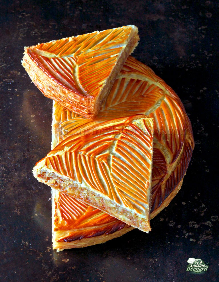 Une tarte ronde avec une croûte dorée au motif de feuilles complexes, partiellement tranchée pour révéler sa garniture en couches de caramel sur un fond sombre.