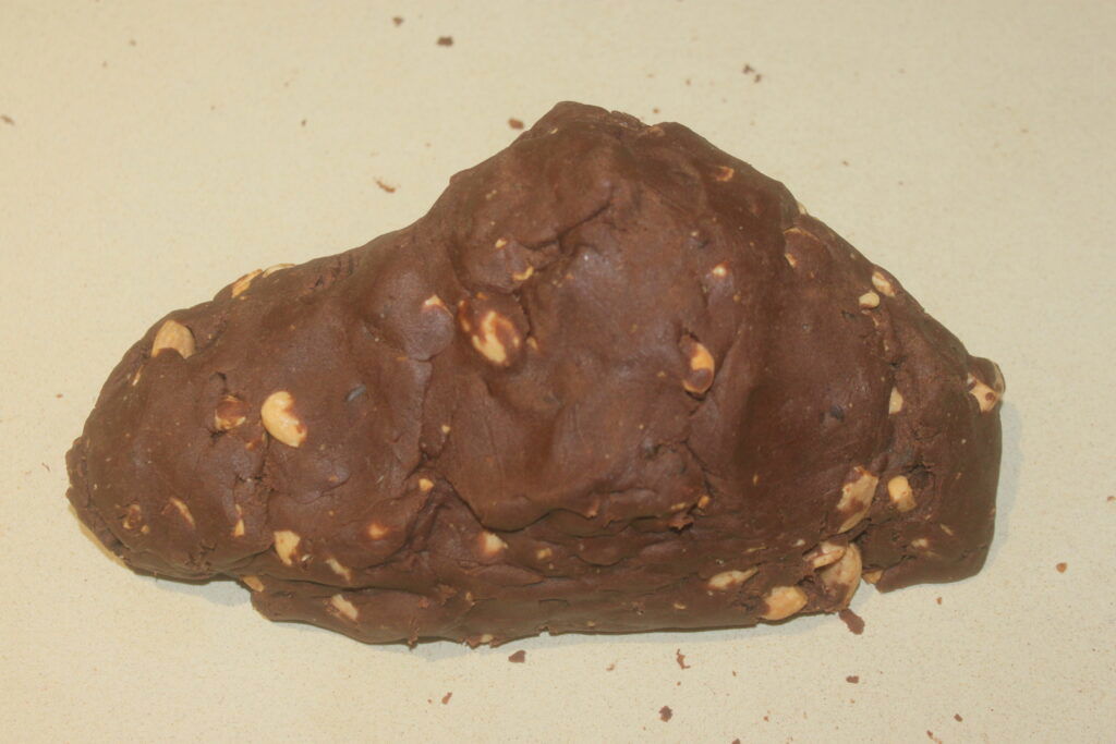 Un morceau de pâte au chocolat brun foncé avec des amandes visibles sur une surface claire.