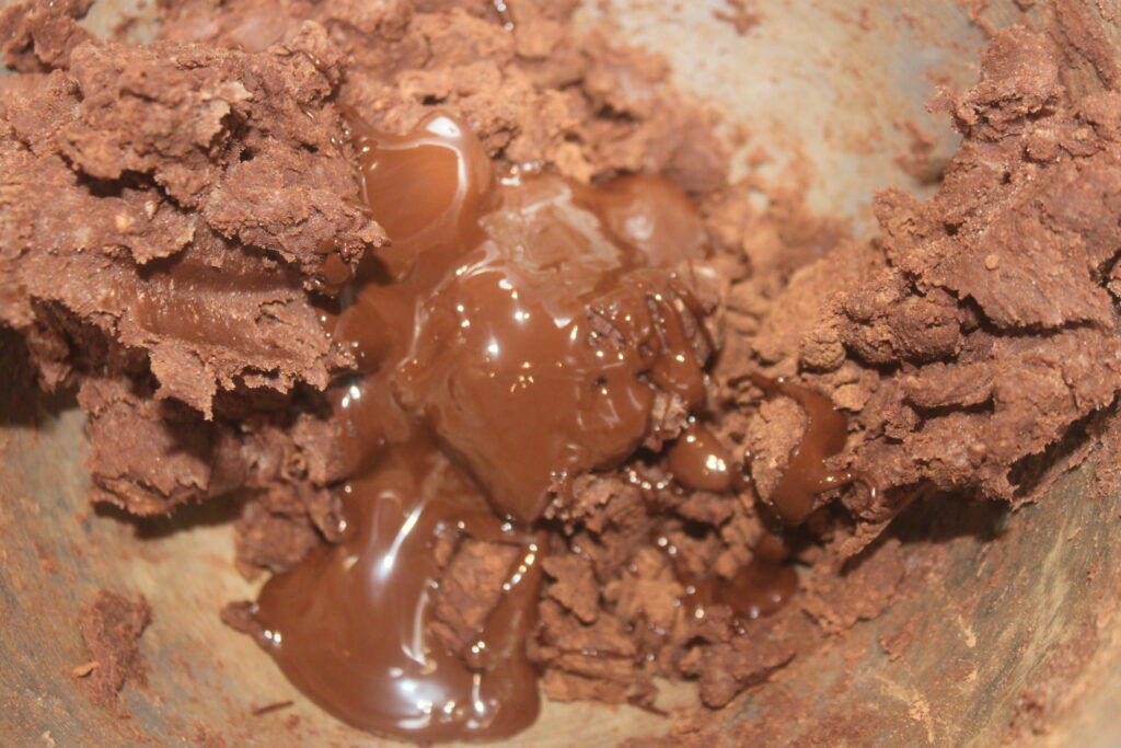Gros plan d'un mélange riche de chocolat et de poudre de cacao mélangés dans un bol, parfait pour confectionner des sablés décadents ou ajouter de la profondeur aux créations au chocolat et aux amandes.