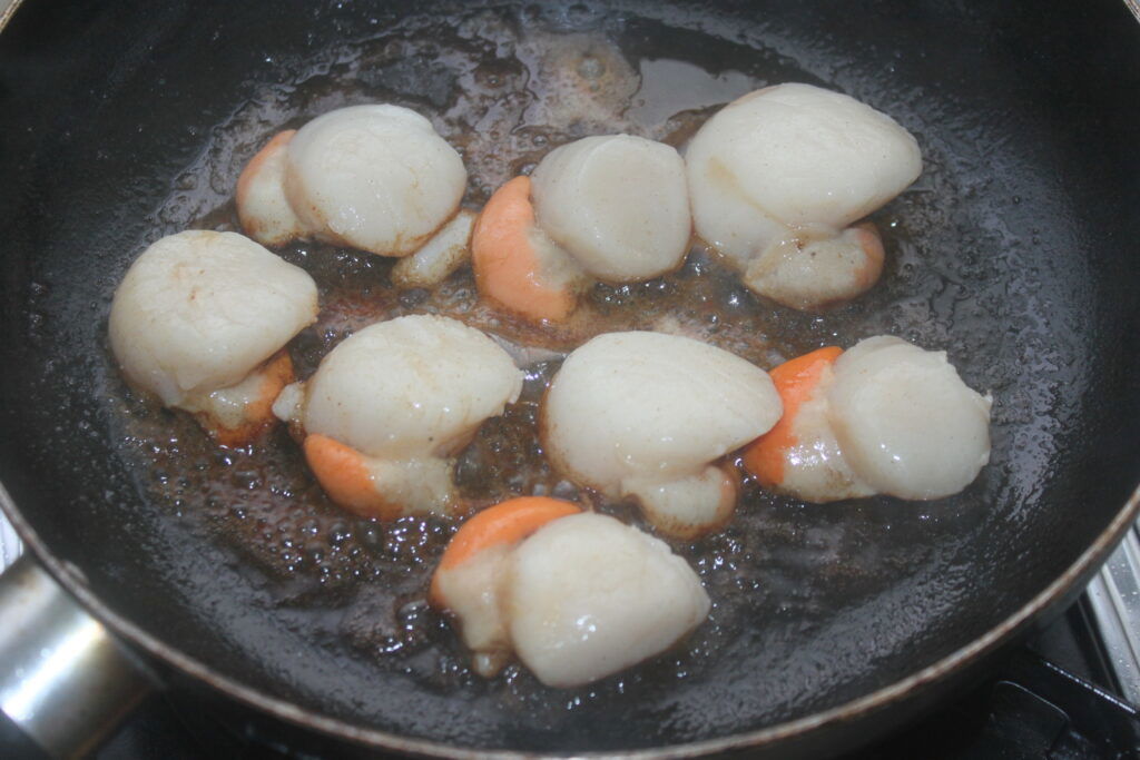 Les coquilles Saint Jacques poêlées grésillent à la poêle, se mêlant à une touche d'huile de cuisson pour une croûte dorée parfaite.