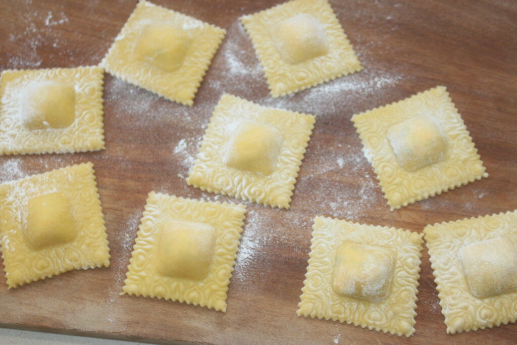 Des carrés de raviolis faits maison, fourrés d'un mélange crémeux de ricotta, sont saupoudrés de farine et disposés sur une surface en bois sur deux rangées.