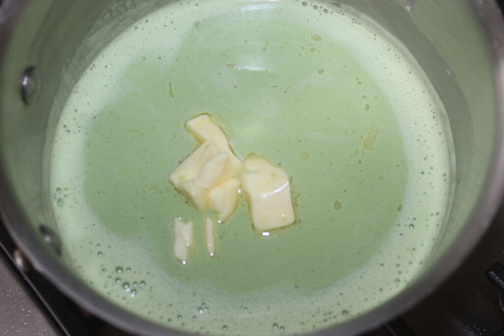 Un pot contenant un mélange liquide vert clair avec plusieurs morceaux de beurre dessus, rappelant la consistance crémeuse du mascarpone.