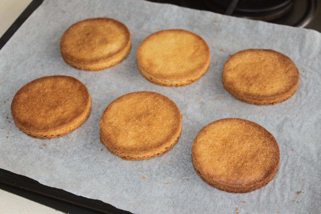 Six biscuits ronds dorés sur une plaque à pâtisserie tapissée de papier sulfurisé, magnifiquement accompagnés d'un côté de chantilly mascarpone pour une touche de gourmandise supplémentaire.