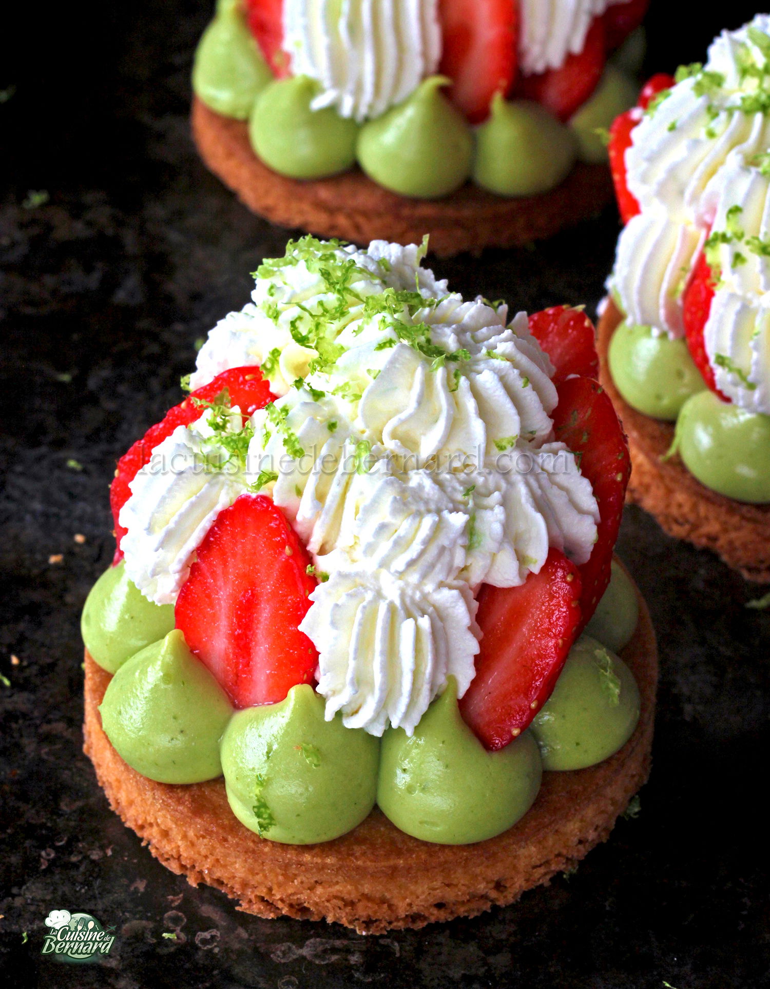 Un dessert composé d'un fond de pâtisserie rond garni de crème verte, de tranches de fraises et de volutes de chantilly mascarpone, garnies de zeste de citron vert.